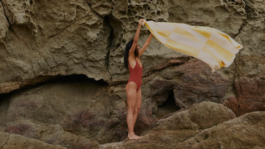 A woman alone on a rock face, holding a yellow checked towel out to the wind