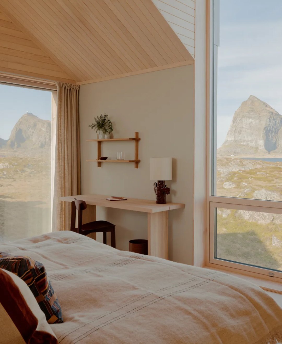 A bedroom with a vaulted timber ceiling and corner windows framing a sea mountain