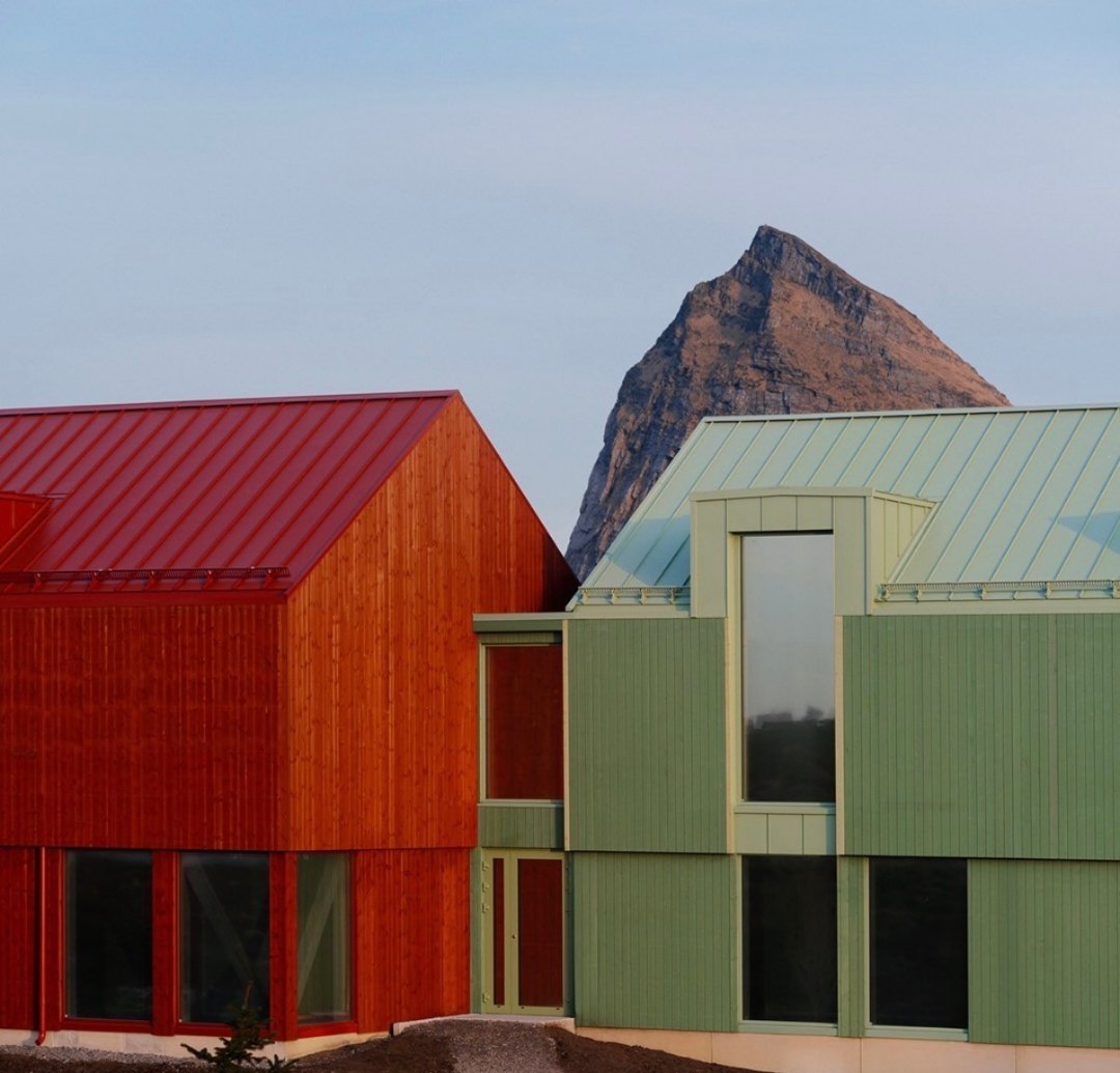 Red and pale green timber buildings with metal roofs, the peak of Tr&aelig;nstaven rising behind them