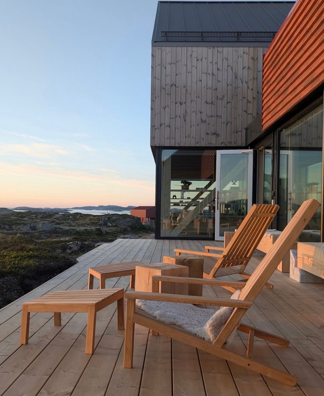 Timber loungers on a deck facing a low sunset over the archipelago