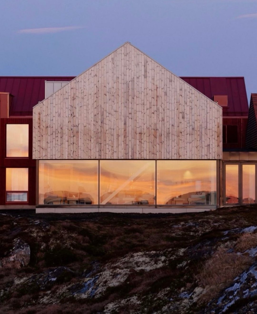 A pale timber gable with a full-width lit window glowing at dusk above dark heath