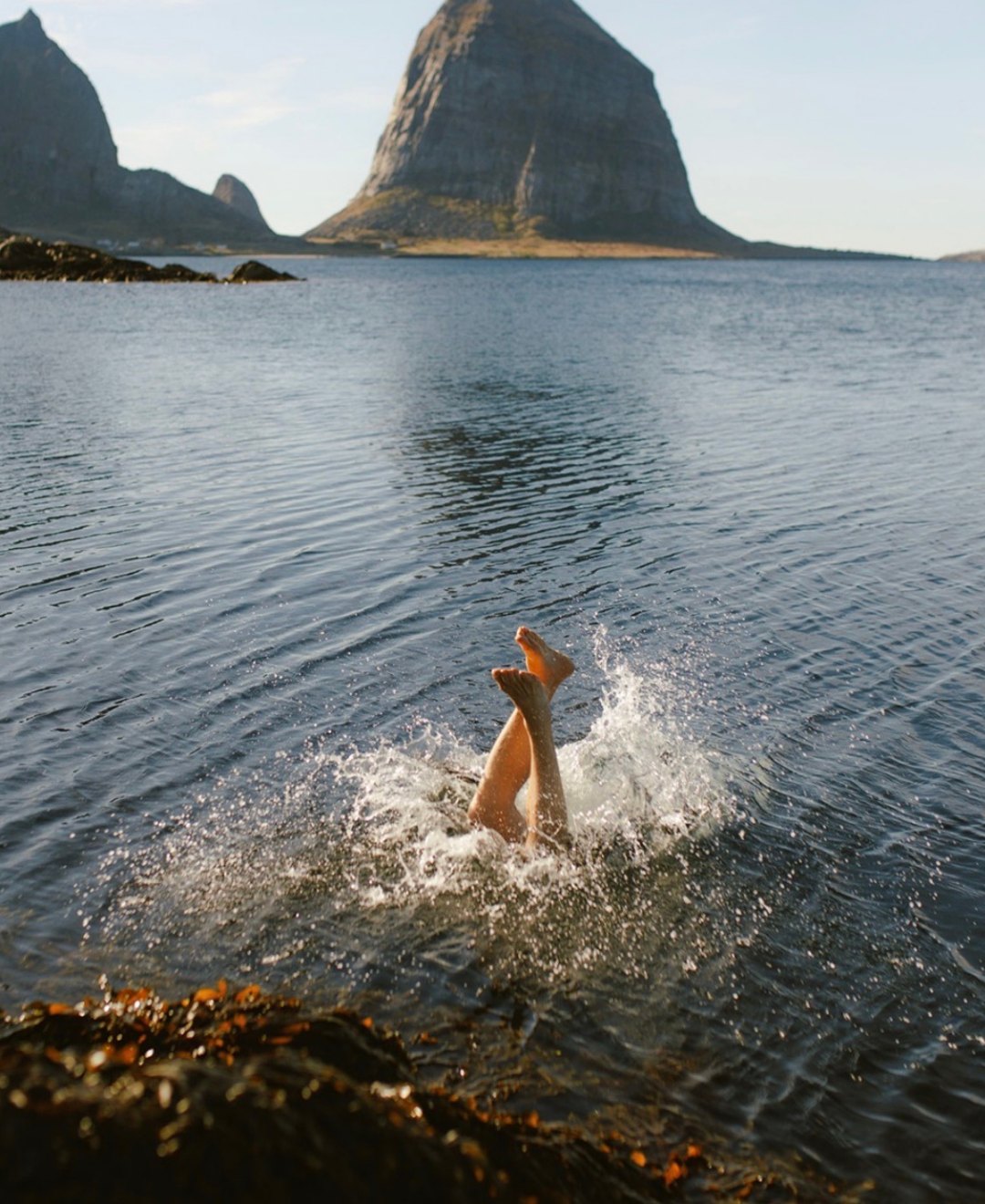 A swimmer diving into clear Arctic water with a steep mountain island behind